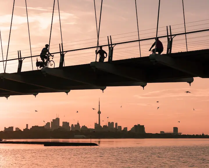 sunset orange sky with Humber Bay Bridge in silhouette along with cyclists, walkers and runners on it and the Toronto skyline in the distance taken by @lianhao_qu