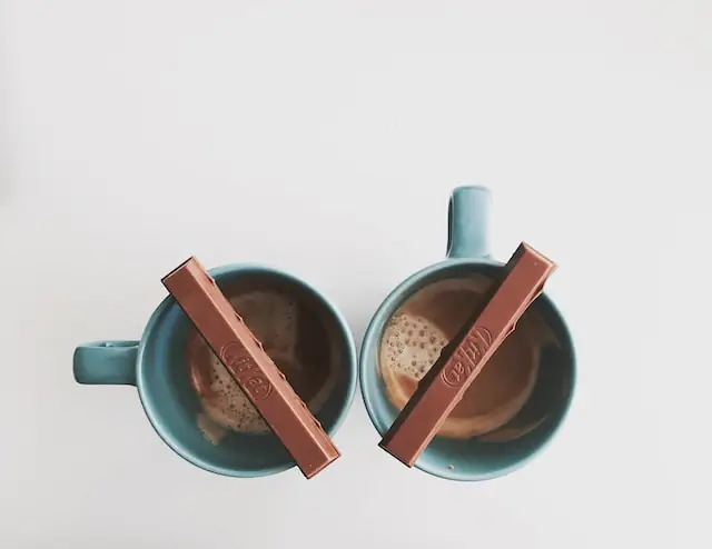 two KitKat pieces one piece
            on each blue coffee mug with either coffee or hot chocolate in the mugs