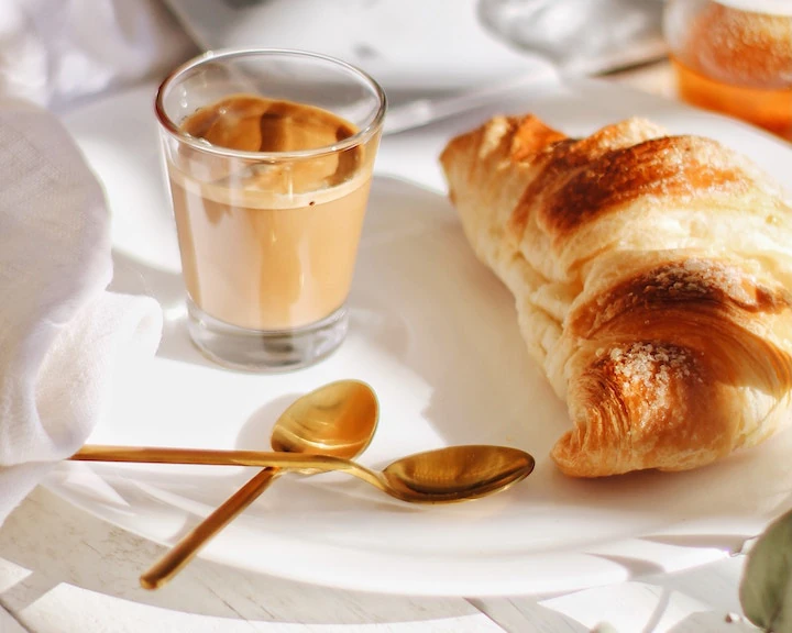 Croissant and milk coffee with some spoons on a white tablecloth