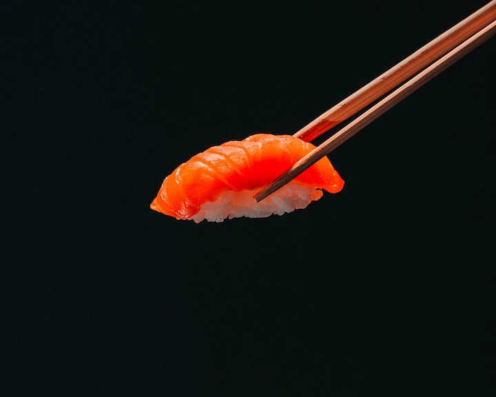 sushi held by wooden chopsticks with a black back drop