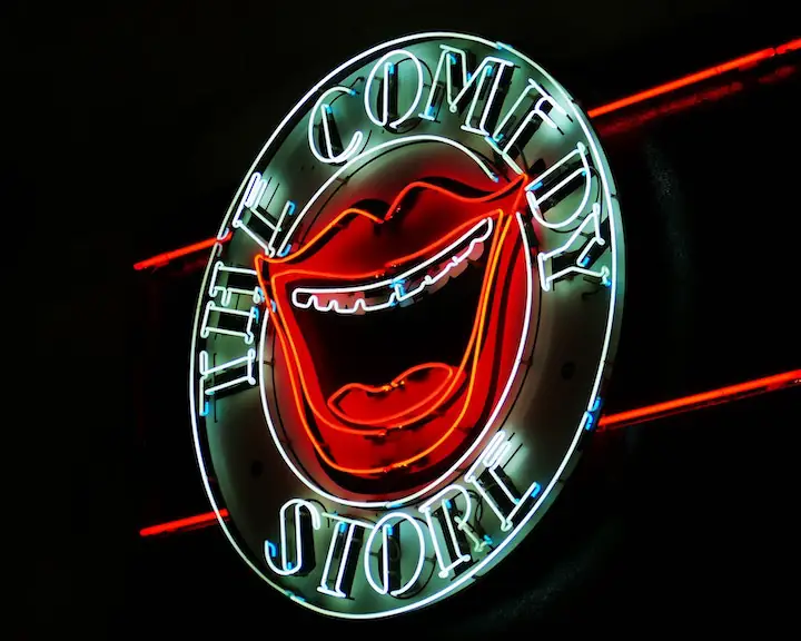 circular neon sign that reads the comedy store with a big smile in the middle