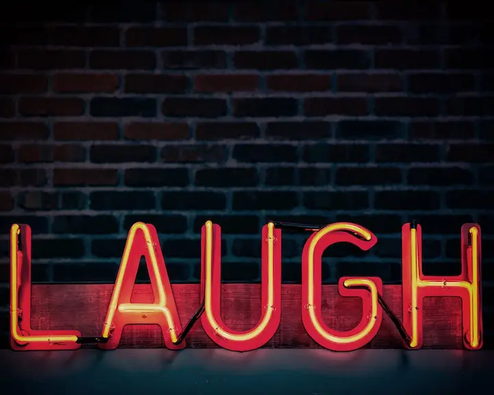 Neon red sign that reads laugh with brick wall in background