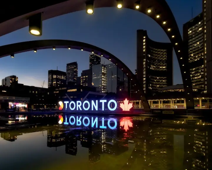 night photo of illuminated Toronto sign at Nathan Phillips Square with reflection in reflection pool by @filipephotographs