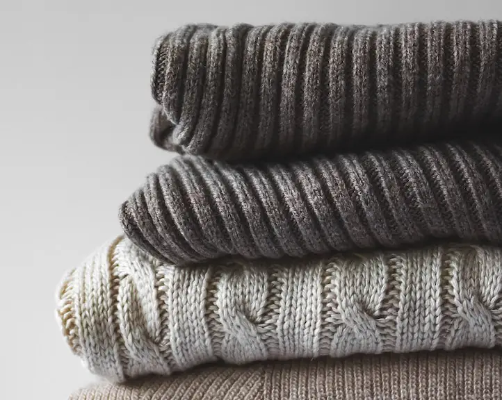 a pile of sweaters in khaki and grey tones